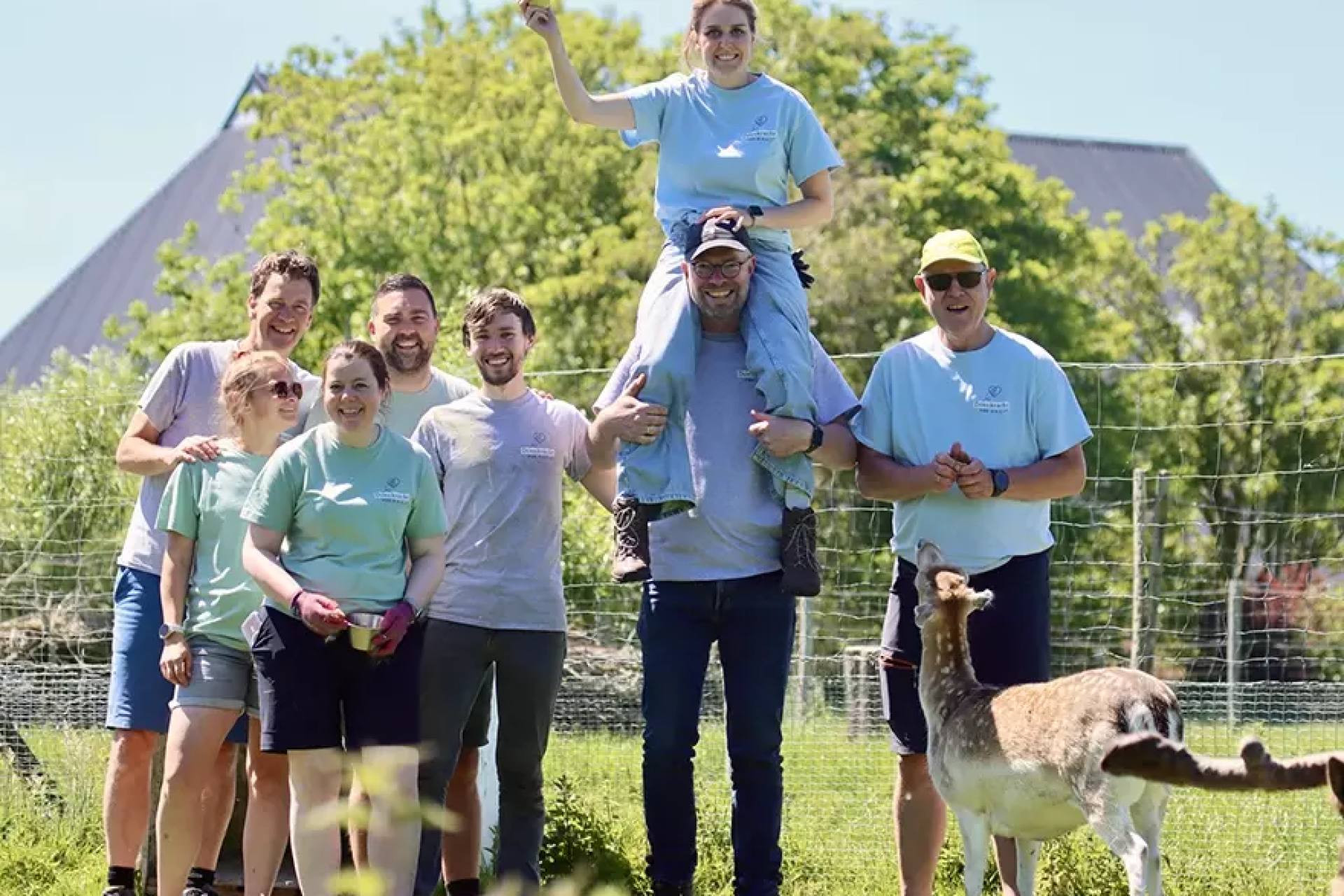 Een groep mensen poseert vrolijk buiten met een hert op de voorgrond.