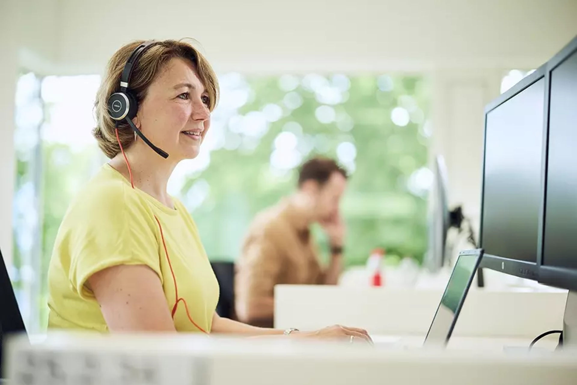 Vrouw met headset werkt aan computer in een kantooromgeving.