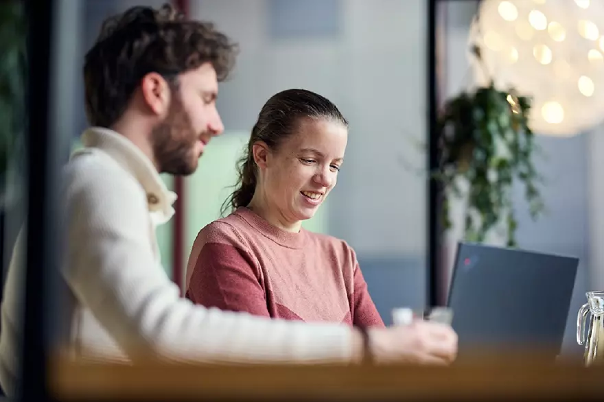 Twee mensen werken samen aan een laptop in een moderne kantooromgeving.