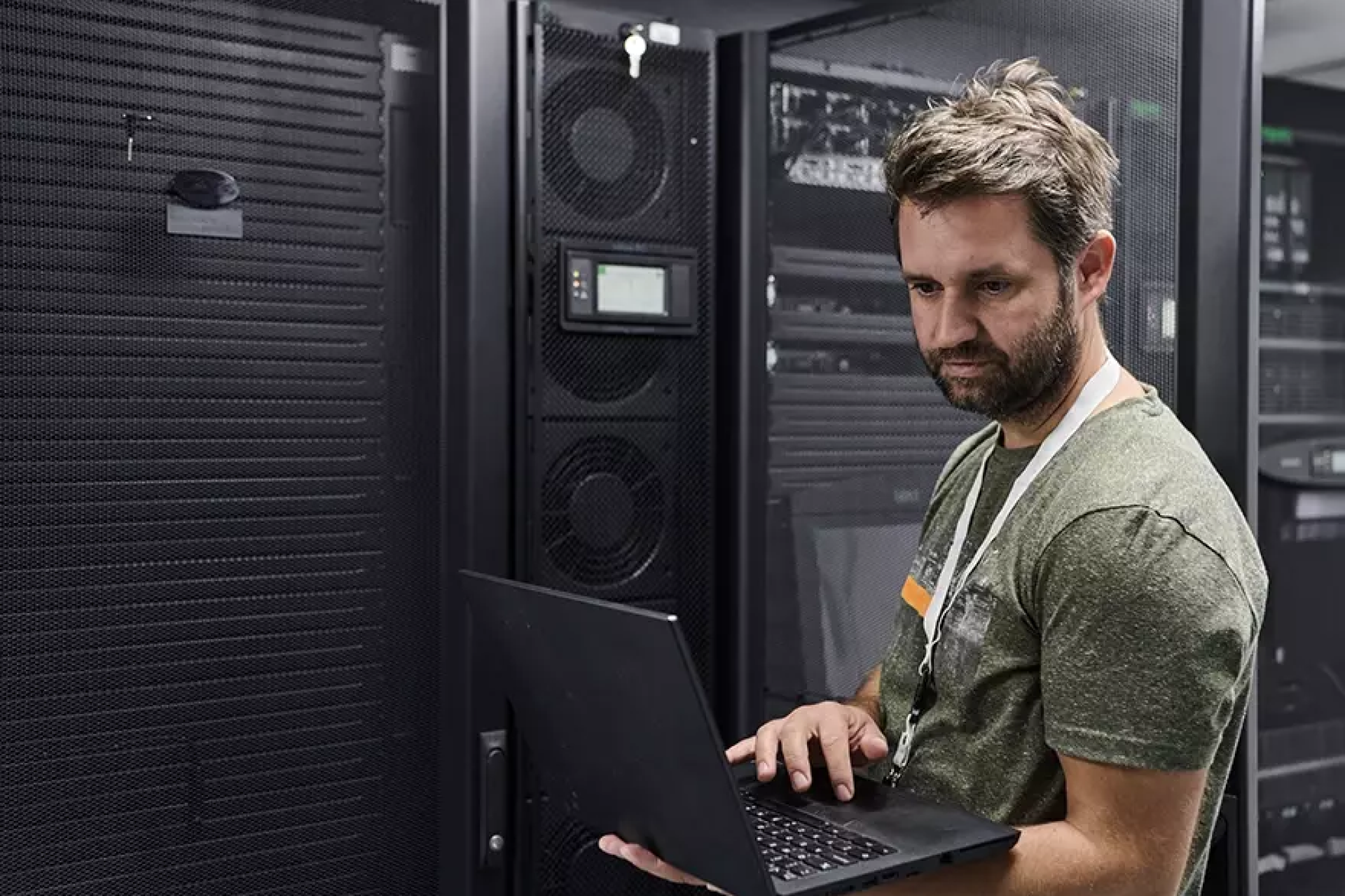 Een man werkt op een laptop in een serverruimte.